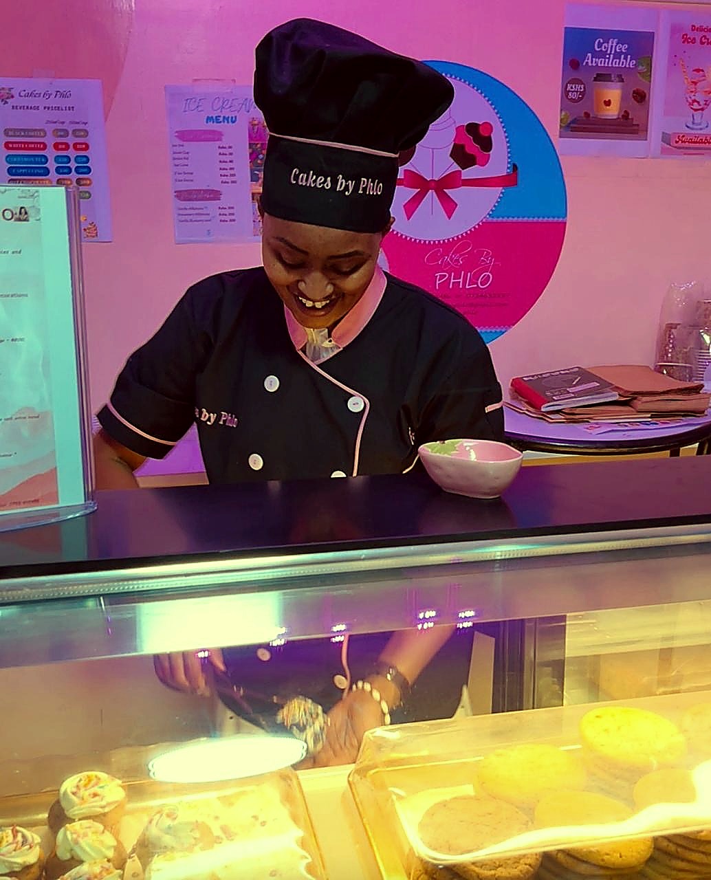 Phlo smiling while working behind the Cakes by Phlo display case